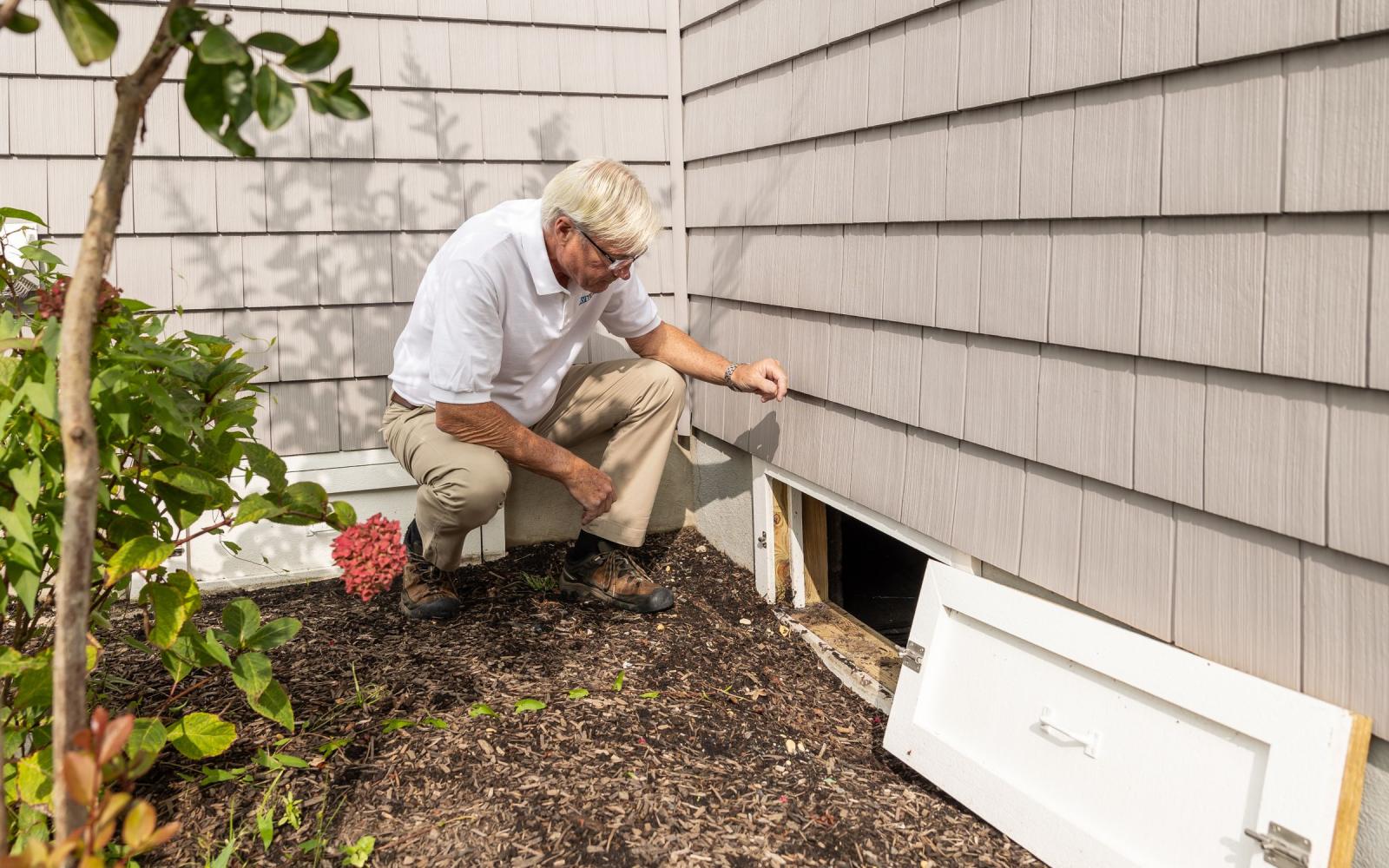 A home inspector checking the crawl space access beside a house
