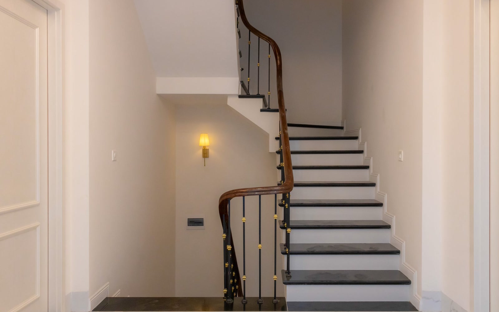 An indoor staircase with a wooden handrail on one side and a light on the wall