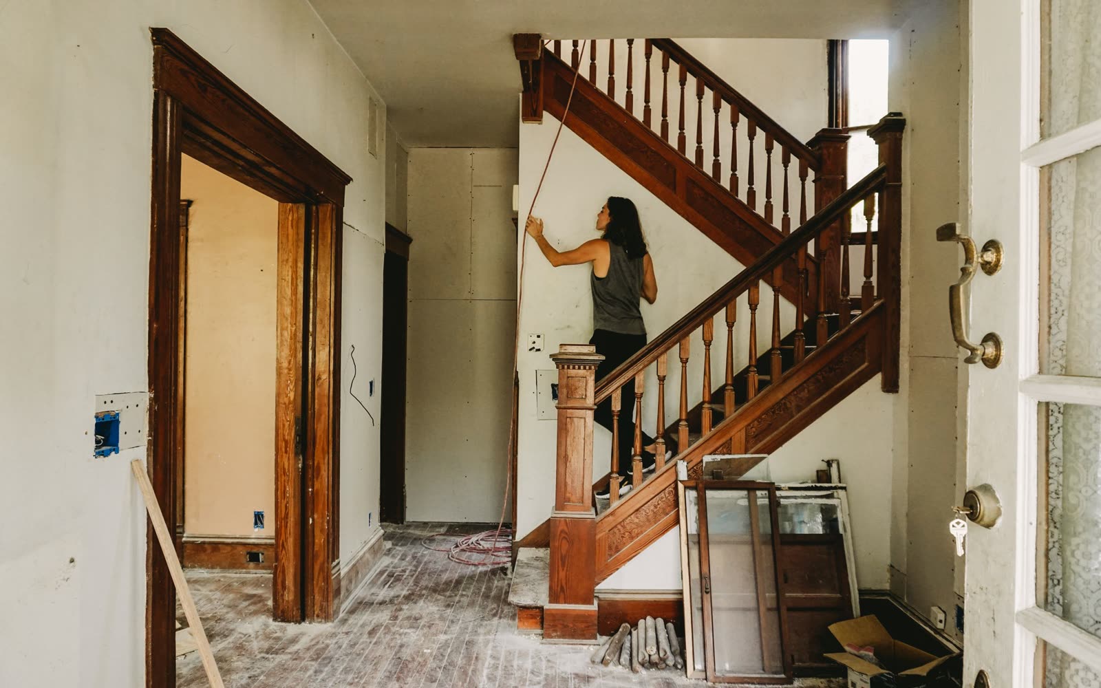 A woman working on an old house mid-renovation, by a wooden staircase