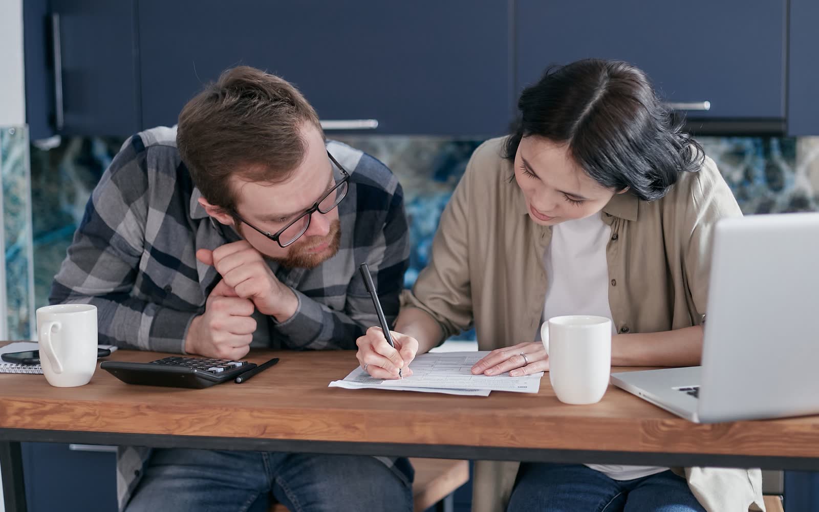 A young couple going over figures with a calculator at the kitchen table