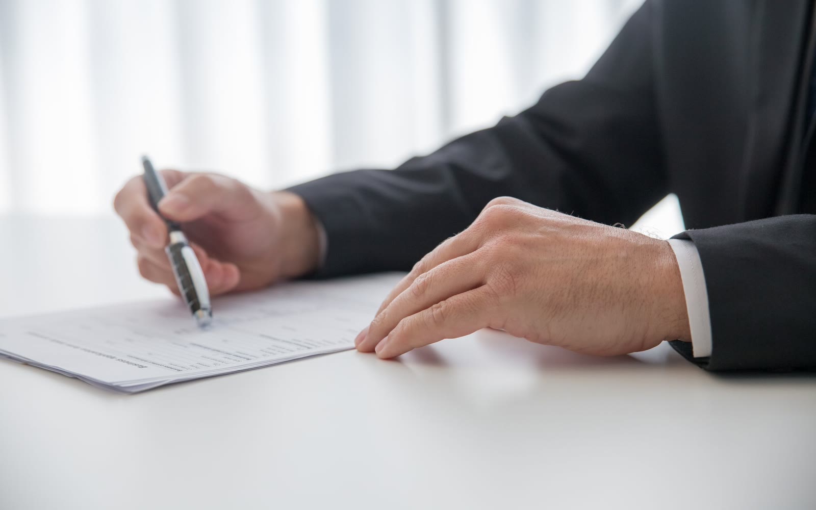 A hand with a pen over papers at a table